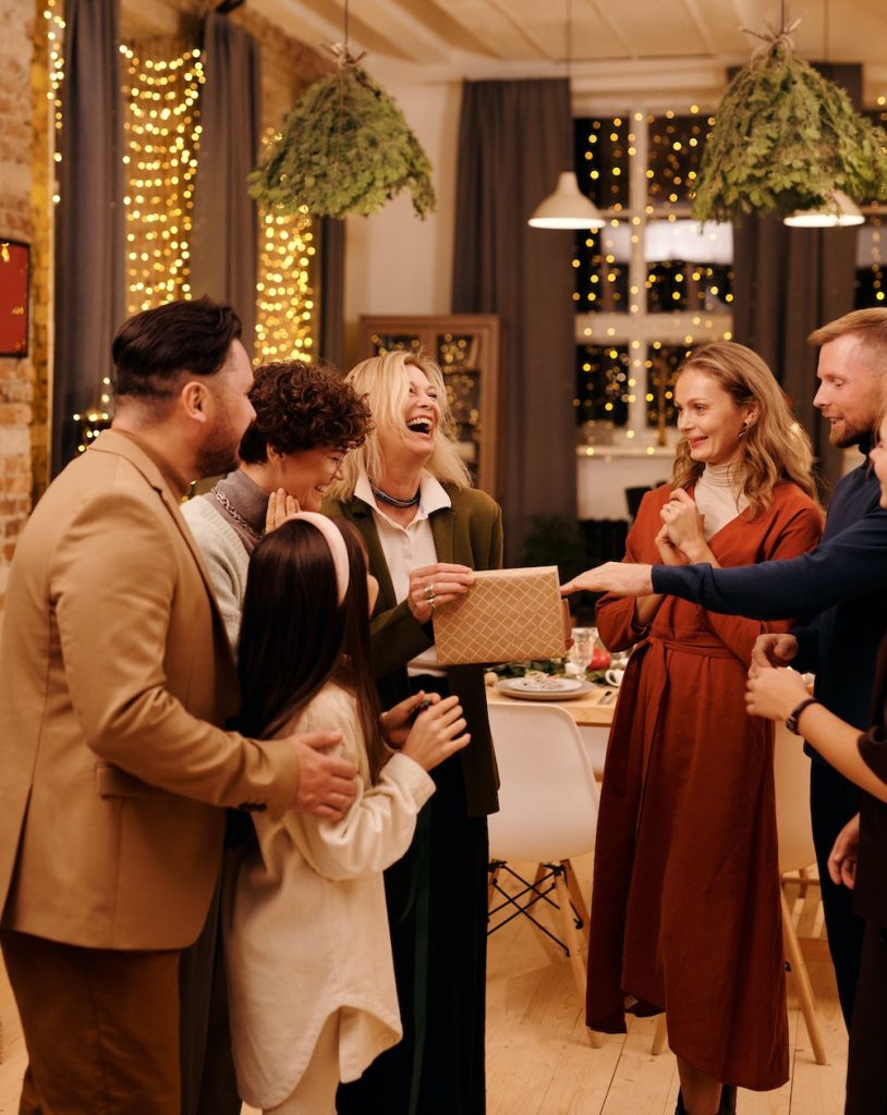 Five Adults and one child laughing during Christmas gathering while looking at a wrapped gift.