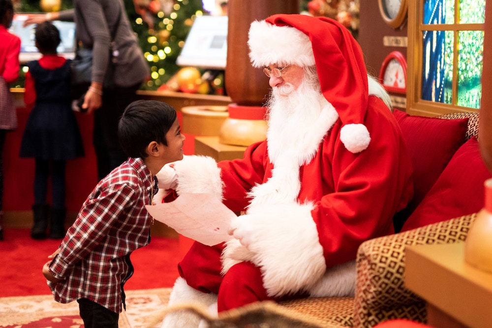 Santa Claus sitting with paper and talking to young boy. 