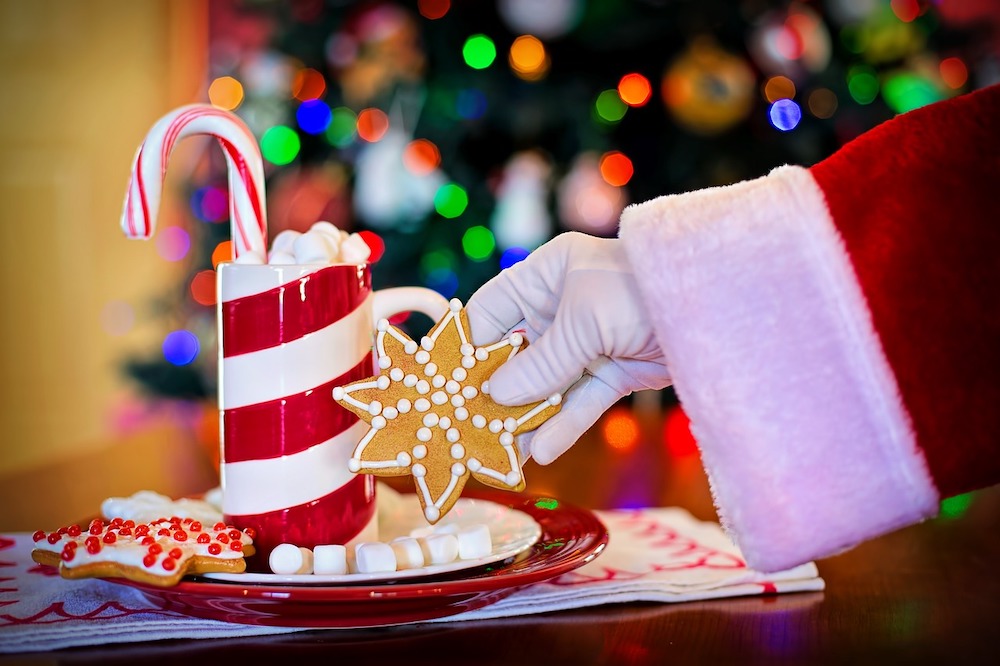 Hand and sleeve of Santa Claus picking up a star cookie from a plate with a glass of cocoa. 
