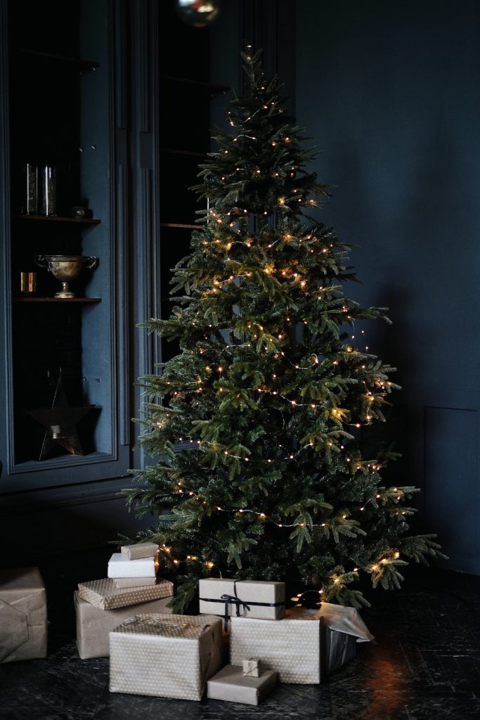 Christmas tree with gold lights against a dark blue wall with presents underneath.
