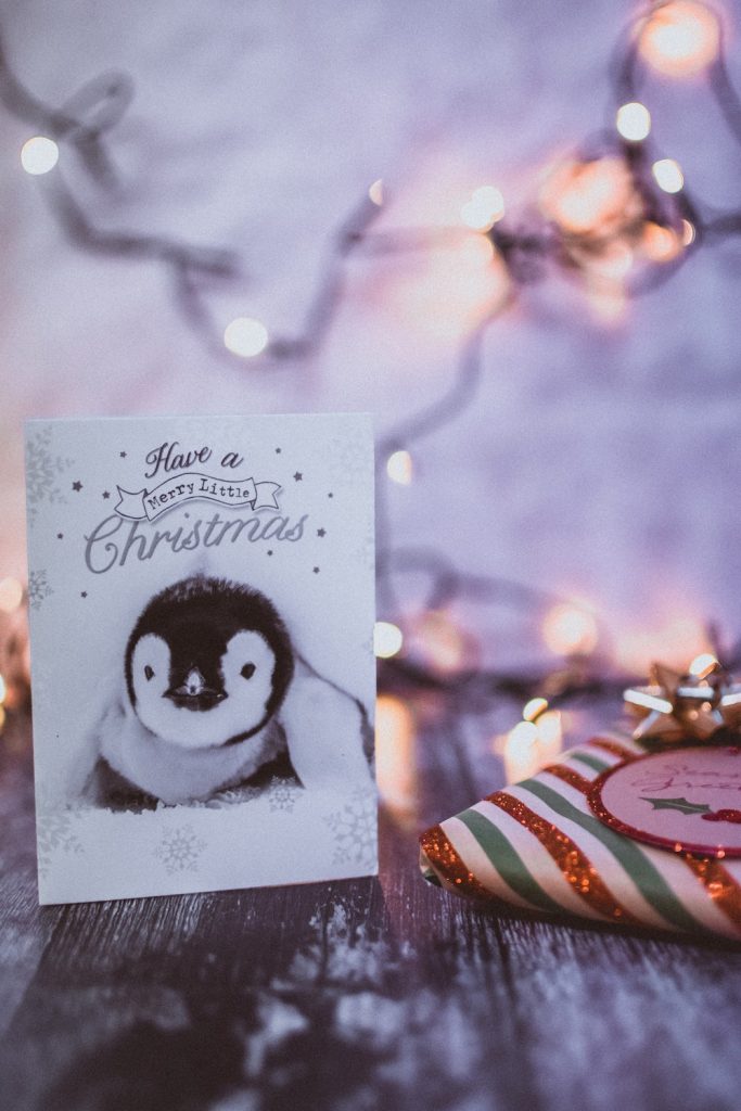 Penguin on a Christmas card with words "have a merry little Christmas" card is sitting on table with present.