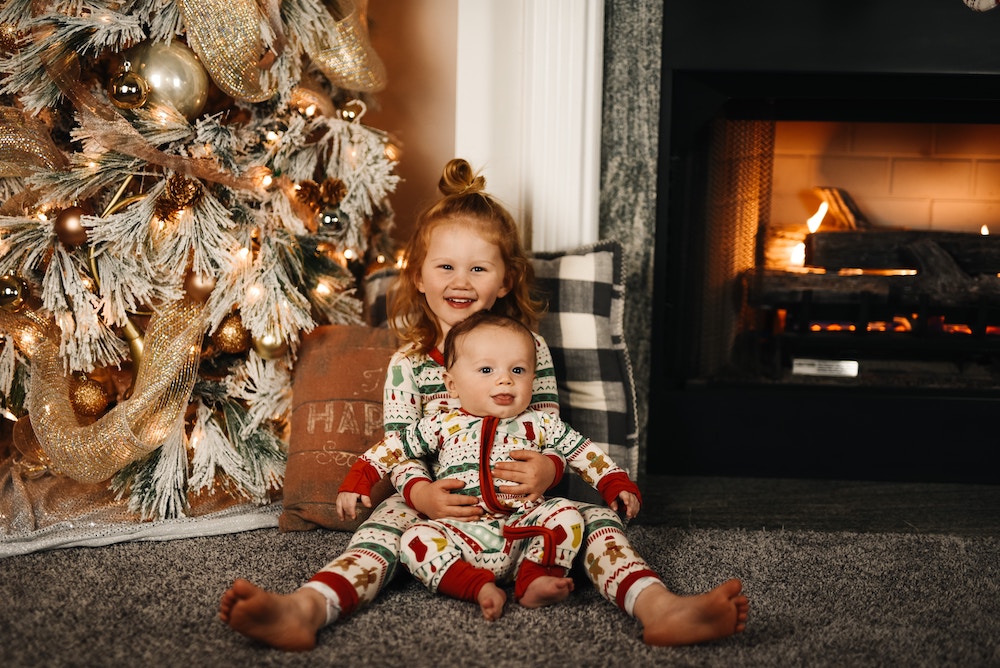 Christmas photo card with girl and boy dressed in same pjs in front of the tree.