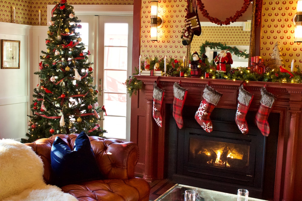 Decorated Christmas tree next to burning fireplace with stockings hanging