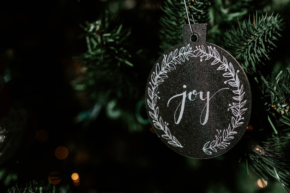 Christmas ornament that is round with word joy inscribed in white, hanging from green branch to show joy of Christmas trivia