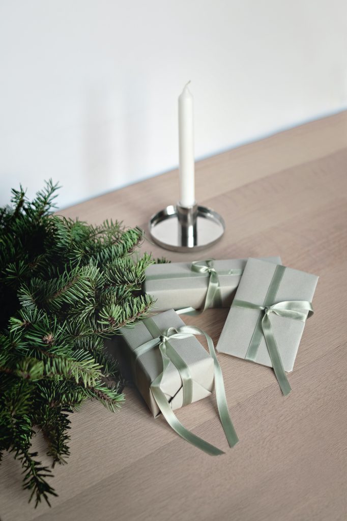 Mini prize gifts for Christmas trivia game on brown table with evergreen branch and silver candlestick with white candle