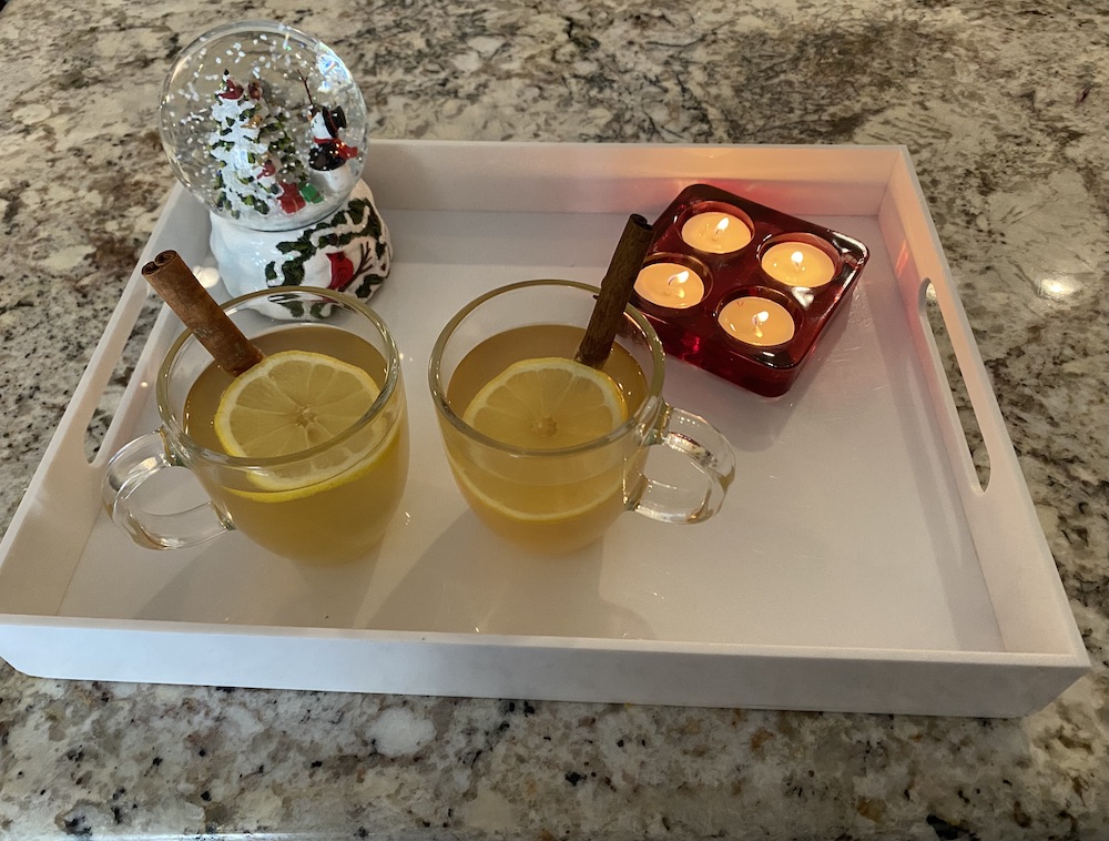 White tray with 2 cups of hot toddy, snowglobe and candles.