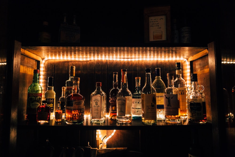Various bottles of whiskey on a lighted shelf.