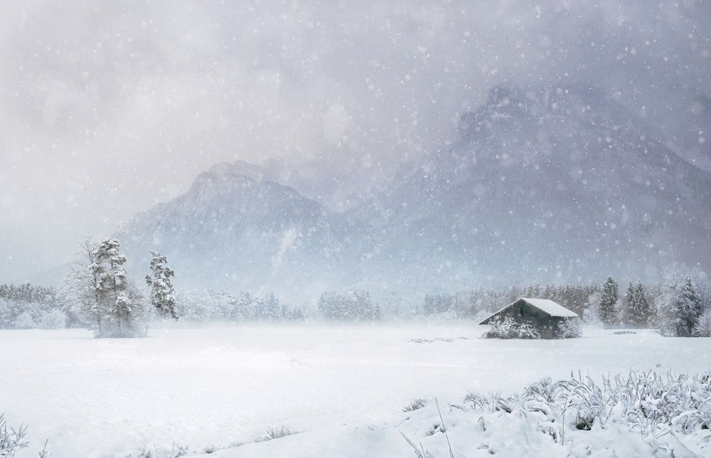 Winter scene with cabin, trees and mountains.