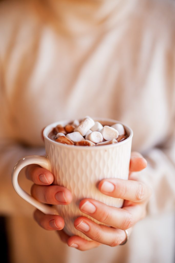 Pair of hands holding mug of hot chocolate with marshmallows.
