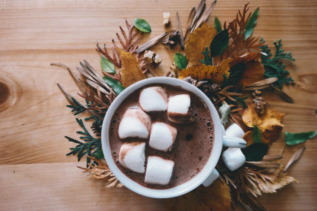 Air shot of cup with hot chocolate and marshmallows sitting on a table with leaves.