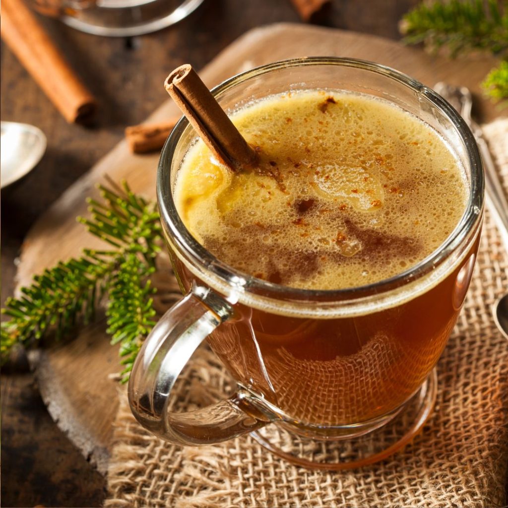 Hot buttered rum in a clear mug next to sprigs of ivy and cinnamon stick