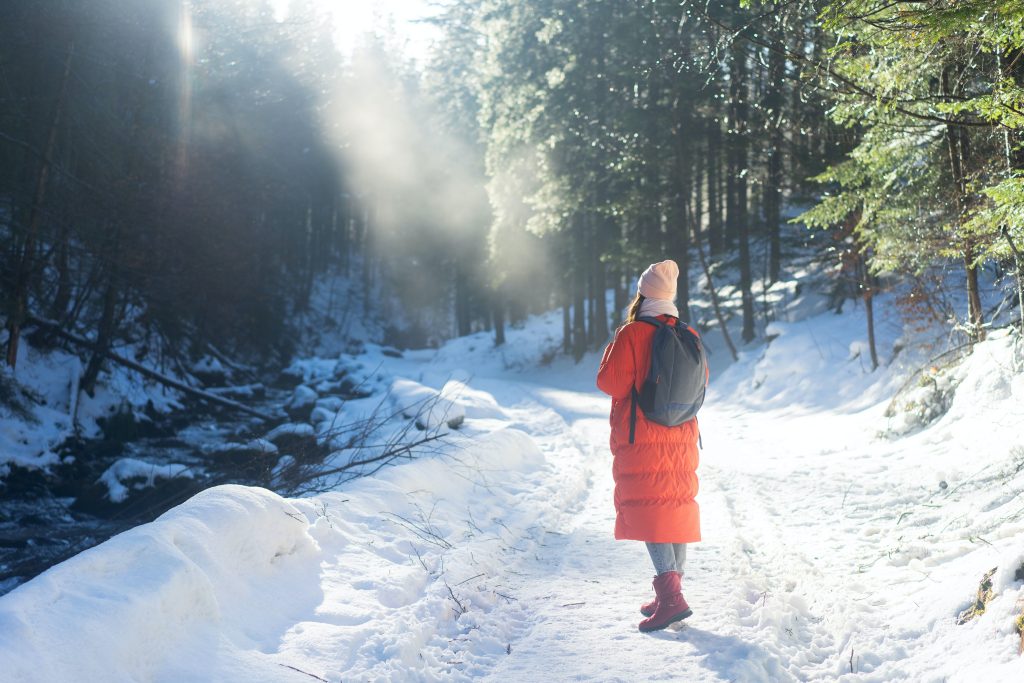 Woman standing on path in the snow covered woods wearing a red parka.