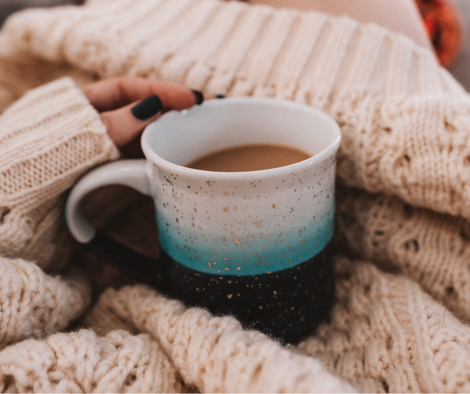 Woman in cozy sweater with mug of coffee to show self care is a way of coping with post holiday blues.
