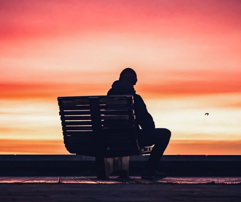 Man sitting on bench reflecting on holidays at sunset.