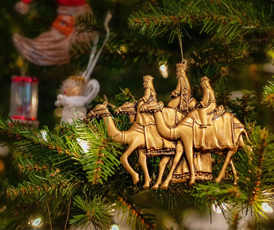 Gold ornament of three kings hanging on tree.