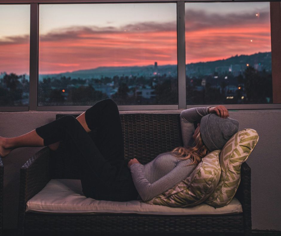 Winter activities for everyone including being alone. Woman sitting on couch looking at sunset.