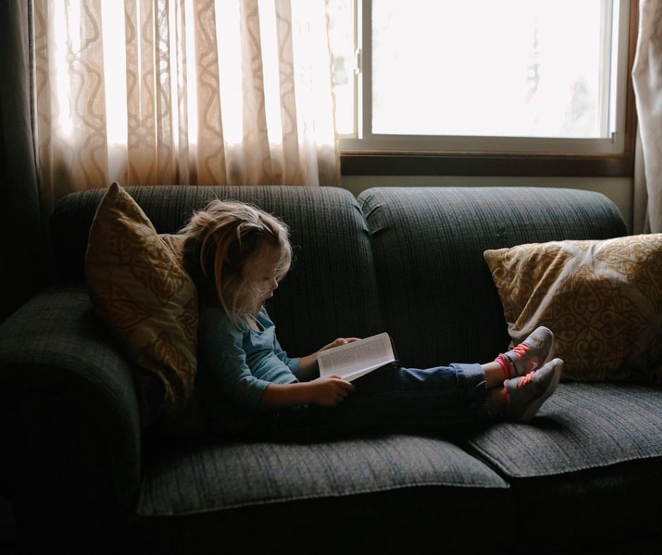 Little girl enjoying winter activity on couch reading a book.