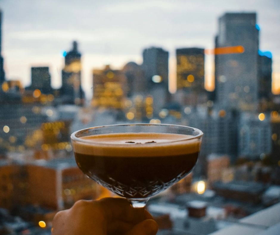Glas with espresso martini recipe held up to window with NYC in view.