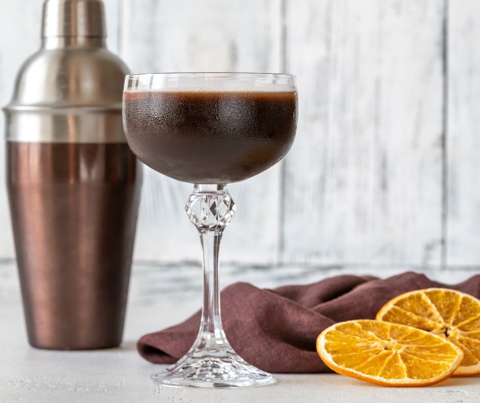 Brown shaker, espresso martini recipe in a glass with orange slices on side. 