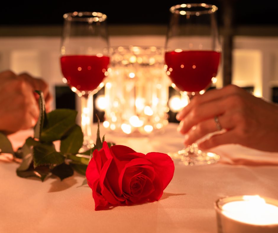 Hands of couple with glasses of wine at candlelit dinner.