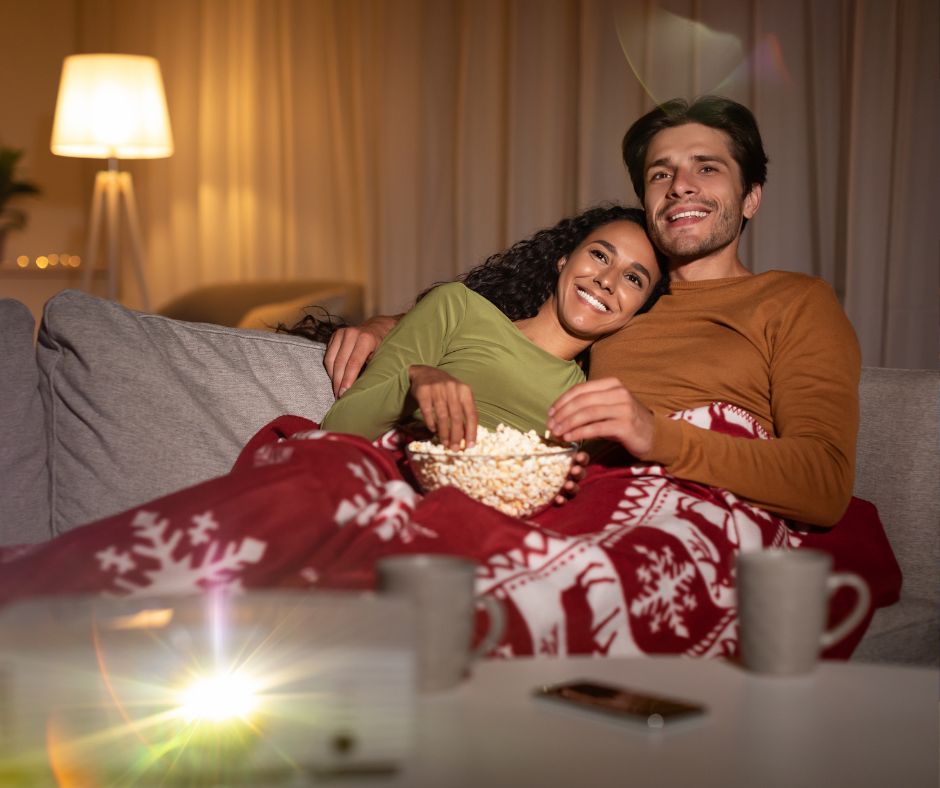 Couple with popcorn with one of the must watch Christmas movies on tv with red and white blanket.