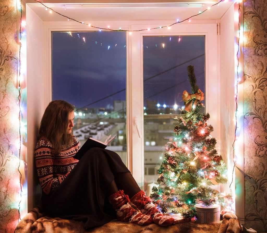 European Christmas tradition of gifting books in Iceland. Shows girl on window edge reading a book with Christmas tree next to her. 